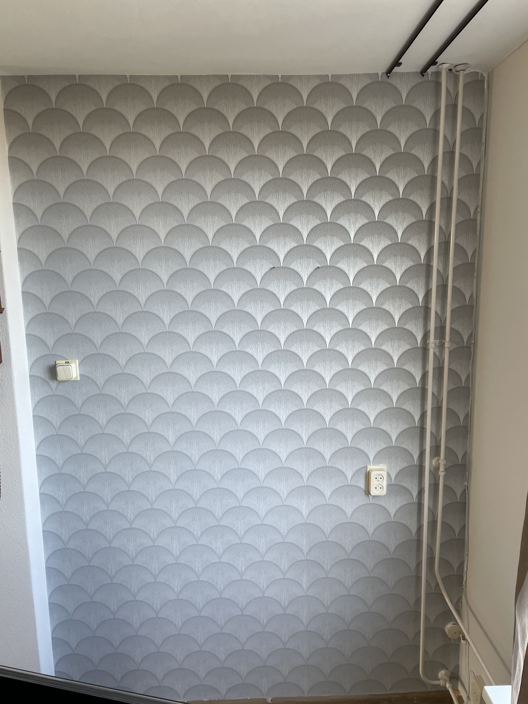 Grijs behang met schelpmotief op een strak afgewerkte wand